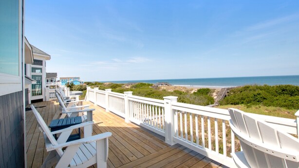 Eine Holzterrasse mit weißen Geländern, die auf einen Strand blickt.