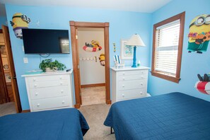 A bedroom with two beds, a dresser, a television, and Minion-themed decorations.