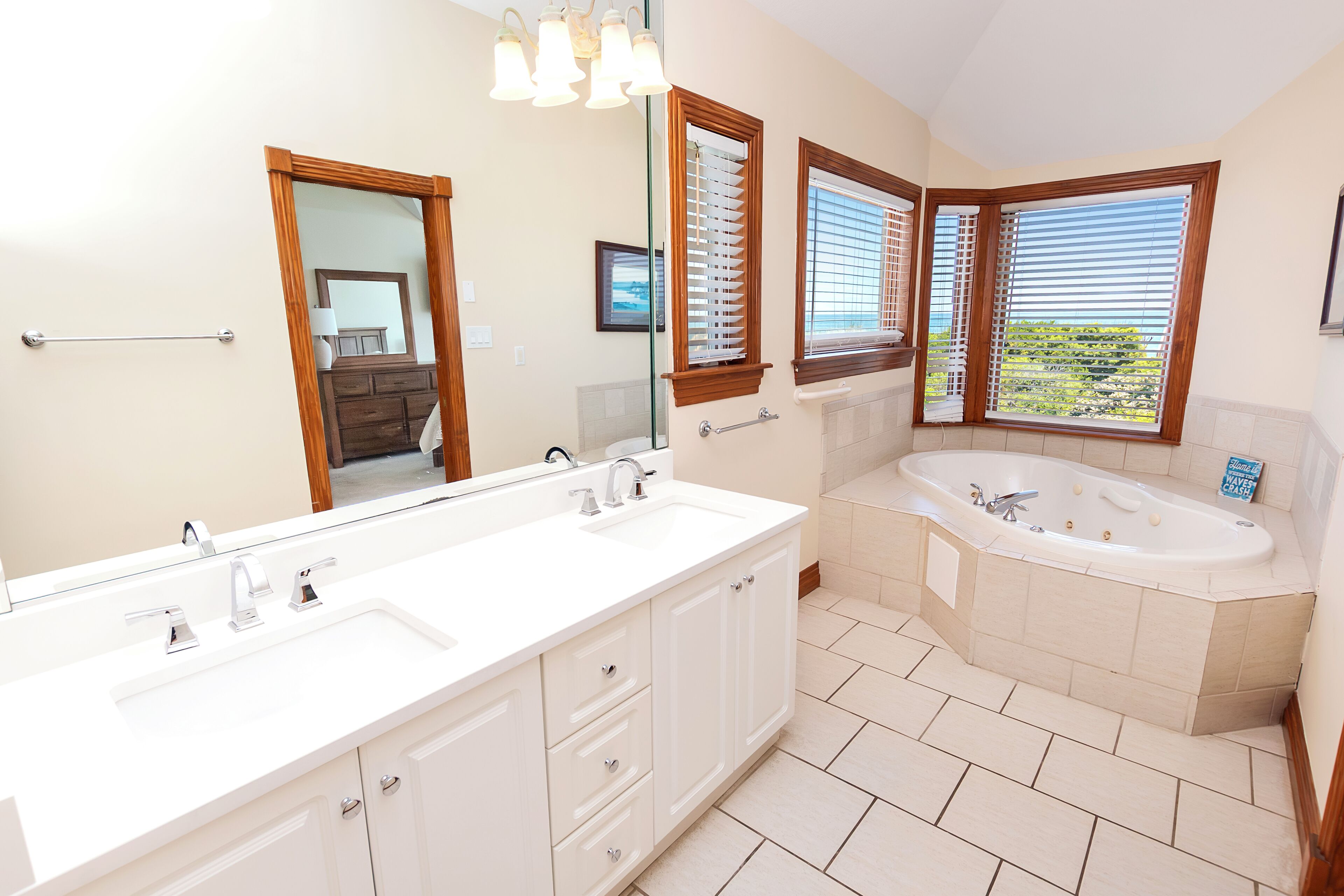 A bathroom with a double sink vanity, a bathtub, and large windows with blinds.