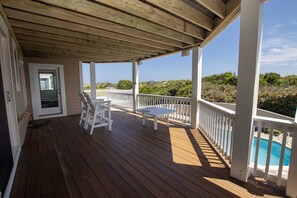 A wooden deck with white railings, a pool, and a door leading to a covered area.