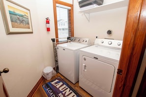 A laundry room with a washer and dryer, a fire extinguisher, and a door with a doormat.