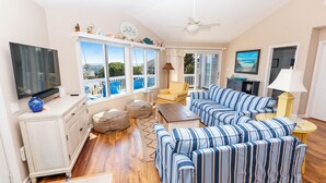 A spacious living room with a large TV, striped sofas, a ceiling fan, and a view of the outdoors. - Oceanside, Private Pool, Hot Tub, Community Pool, CD7, Sandfiddler Lodge (Duck)