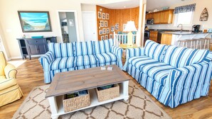 A living room with striped sofas, a wooden coffee table, and a kitchen in the background. - Oceanside, Private Pool, Hot Tub, Community Pool, CD7, Sandfiddler Lodge (Duck)