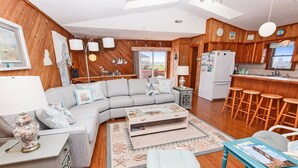 A cozy living room with a sofa, coffee table, and a dining area with stools. - Oceanside, Close to beach, Sunroom, Carport, SNH351, Sea Sharp (Nags Head)