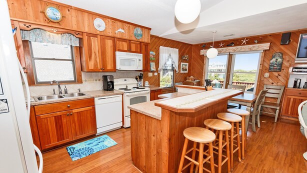 A kitchen with wooden cabinets, a microwave, a sink, and a bar area with stools. - Oceanside, Close to beach, Sunroom, Carport, SNH351, Sea Sharp (Nags Head)