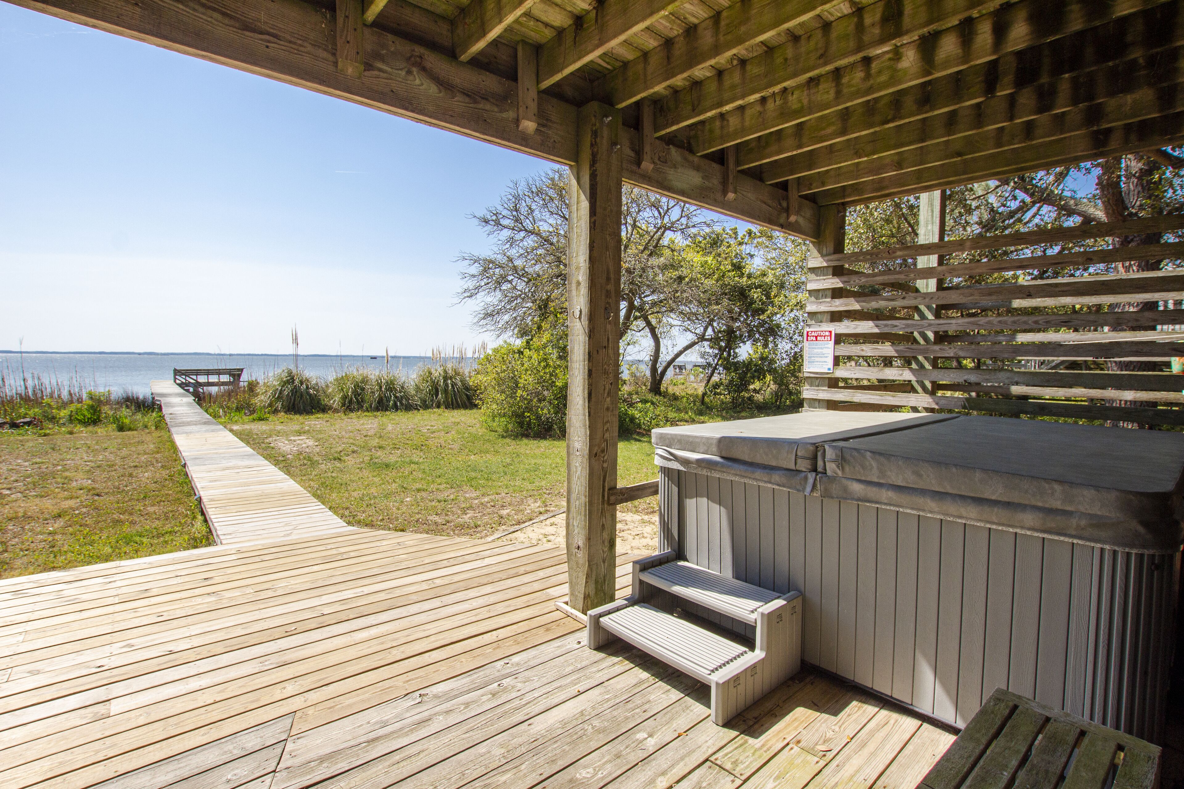 A wooden deck leading to a hot tub area with a view of the water.