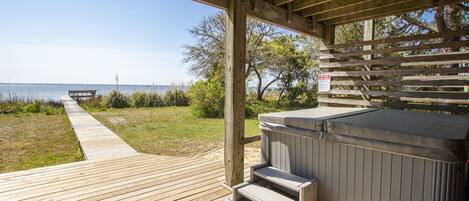 A wooden deck leading to a hot tub area with a view of the water.