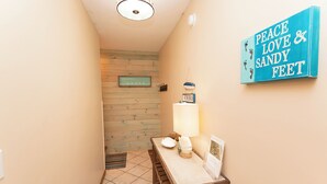 A hallway with a wooden wall, a tiled floor, a table with a lamp, and a sign that reads "Peace Love & Sandy Feet". - Soundfront, Priv Dock, Sound Views, Sun Deck, SA425, Sound Mind (Duck)
