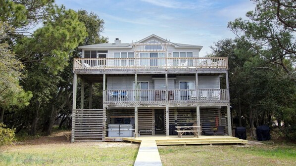 A two-story wooden house with a balcony on the upper floor, a front porch, and a small deck area.
