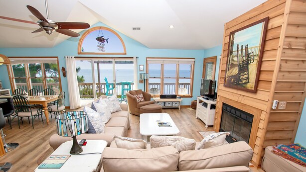 A spacious living room with a large sofa, a coffee table, and a television. There is a balcony with a view of the ocean. - Soundfront, Priv Dock, Sound Views, Sun Deck, SA425, Sound Mind (Duck)