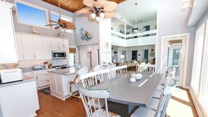 A spacious kitchen with white cabinetry, a central island, and a dining area with white chairs. - OCEANFRONT, Private Pool, Ocean Views, Beach Walkway, Hot Tub, WL1035, PiraSea (Corolla)