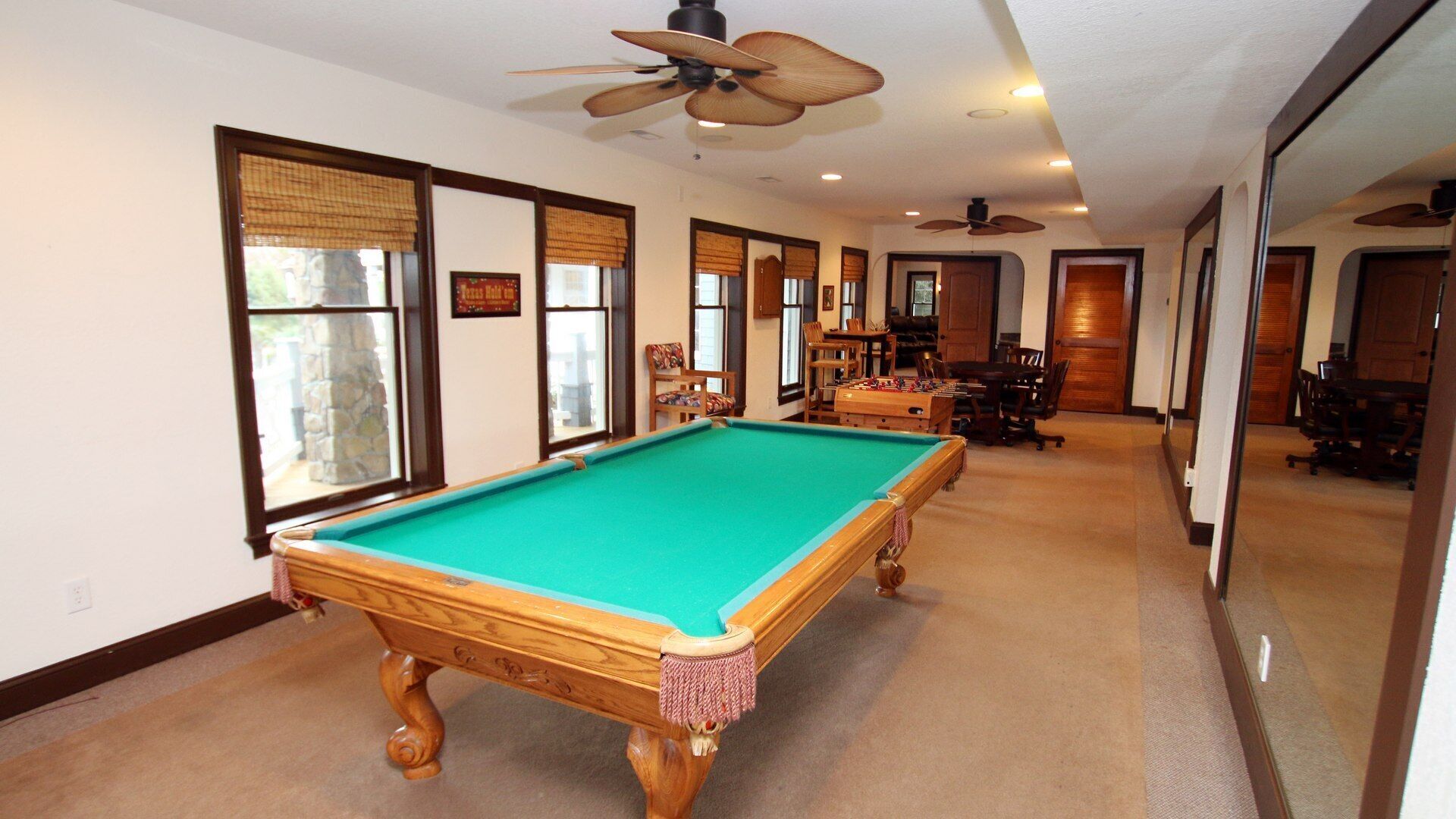 A pool table in a room with large windows, ceiling fans, and a dining area.