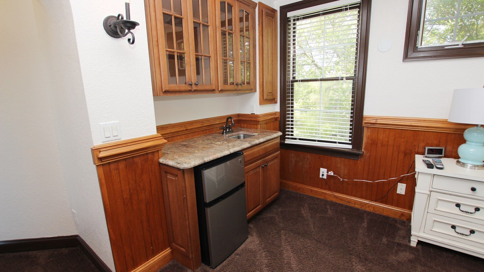 A compact kitchen with wooden cabinets, a built-in dishwasher, and a window with blinds.