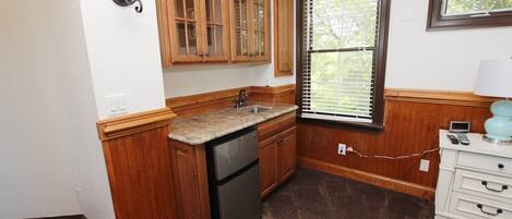 A compact kitchen with wooden cabinets, a built-in dishwasher, and a window with blinds.