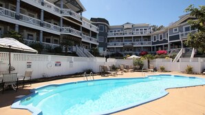 A swimming pool area with lounge chairs and umbrellas, surrounded by a white fence. - Soundside, Priv Pool, H Tub, ELEV, Rec Rm, Theatr Rm, FR1, The Drake (Duck)