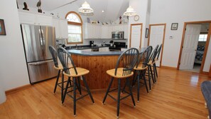 A kitchen with a central island, wooden chairs, a refrigerator, and a microwave.