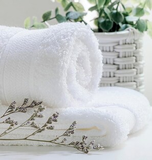 Una toalla blanca enrollada, una cesta tejida y flores de lavanda secas.