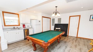 A pool table in a room with a kitchen area, a door, and a ceiling light fixture.