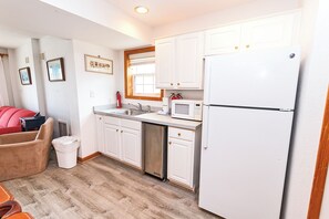 A compact kitchen with white cabinets, a stainless steel sink, a microwave, and a white refrigerator.