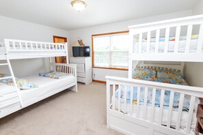 Ein Kinderzimmer mit Etagenbetten, einem Fernseher, einer Kommode und einem Fenster mit Jalousien.