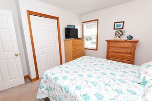 A bedroom with a bed, dresser, television, and a window with blinds.