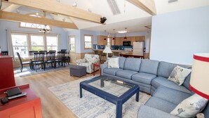 A spacious living room with a large sofa, a glass coffee table, and a dining area with chairs and a table.