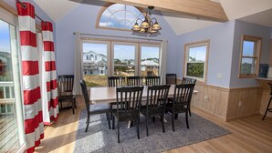 A dining area with a table and chairs, large windows, and a view of houses.