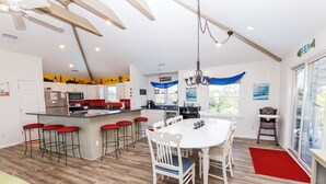 A spacious kitchen with a central island, bar stools, and a dining table with chairs. - Semi-Oceanfront, Rec Room, Private Pool, Ocean Views, WL1092, Maritime (Corolla)
