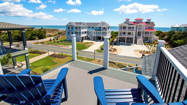 A balcony with blue chairs overlooking a beachfront property with multiple buildings and a clear sky. - Semi-Oceanfront, Rec Room, Private Pool, Ocean Views, WL1092, Maritime (Corolla)