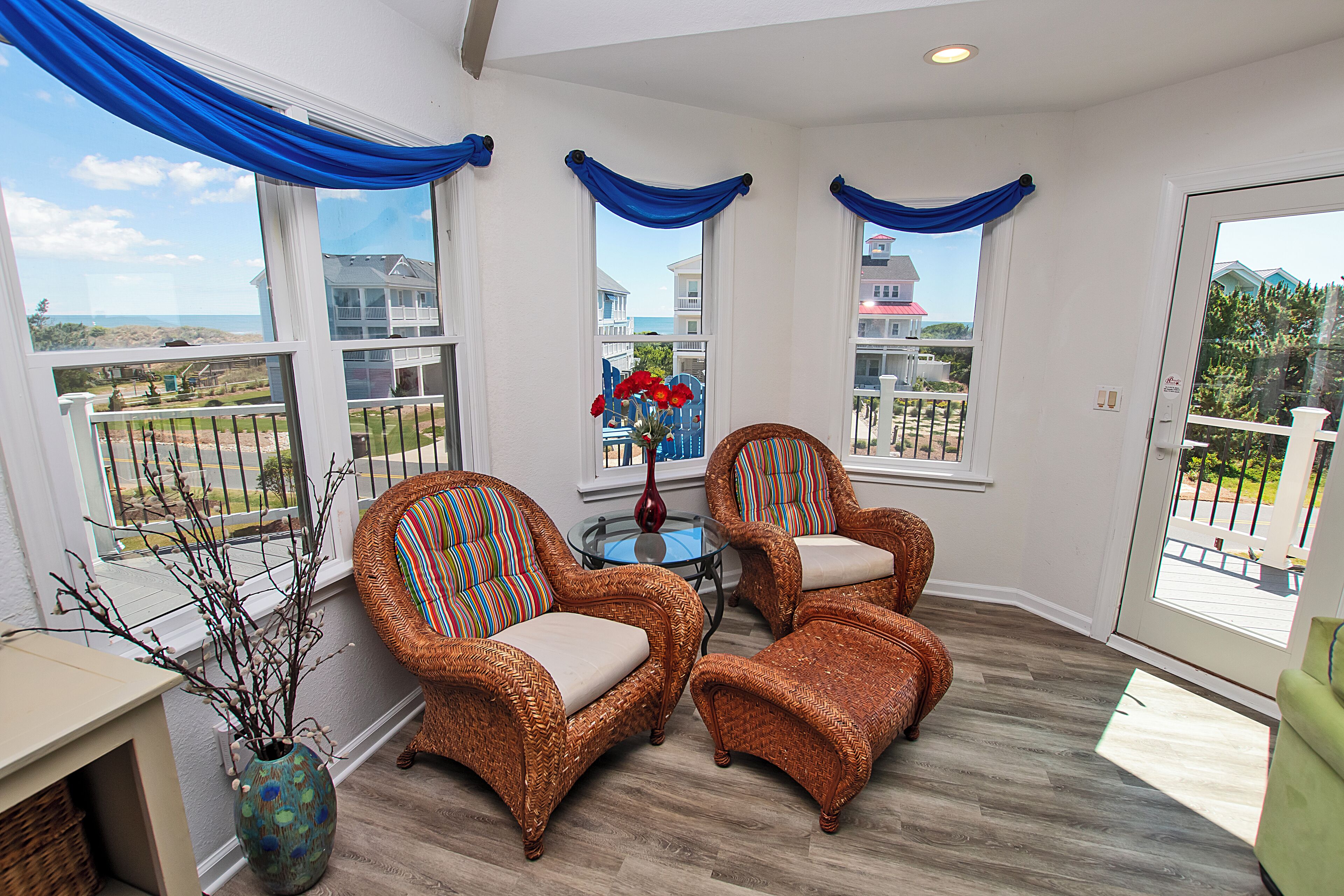 A sunlit room with wicker furniture, large windows, and a view of the ocean.