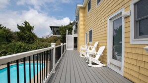 A wooden deck with a pool, white chairs, and a staircase leading to a balcony. - Semi-Oceanfront, Rec Room, Private Pool, Ocean Views, WL1092, Maritime (Corolla)
