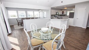 A modern kitchen with white cabinets, a central island, and a dining area with white chairs and a glass table. - Semi-Oceanfront, Private Pool with Cabana! Ocean Views! Pool Table, 126, Newmania (Corolla)