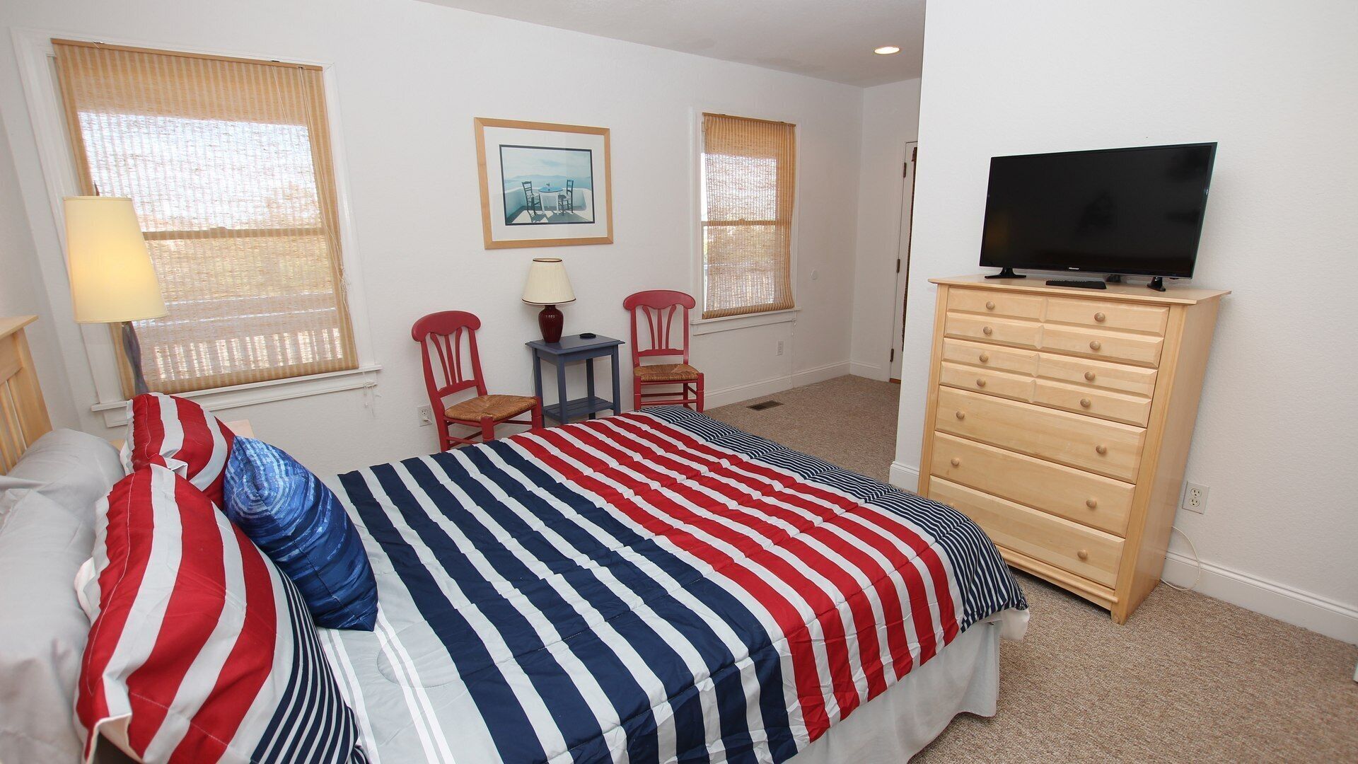 A bedroom with a bed, a dresser, a television, and two chairs.
