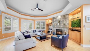 A spacious living room with a fireplace, a ceiling fan, and a stone accent wall.