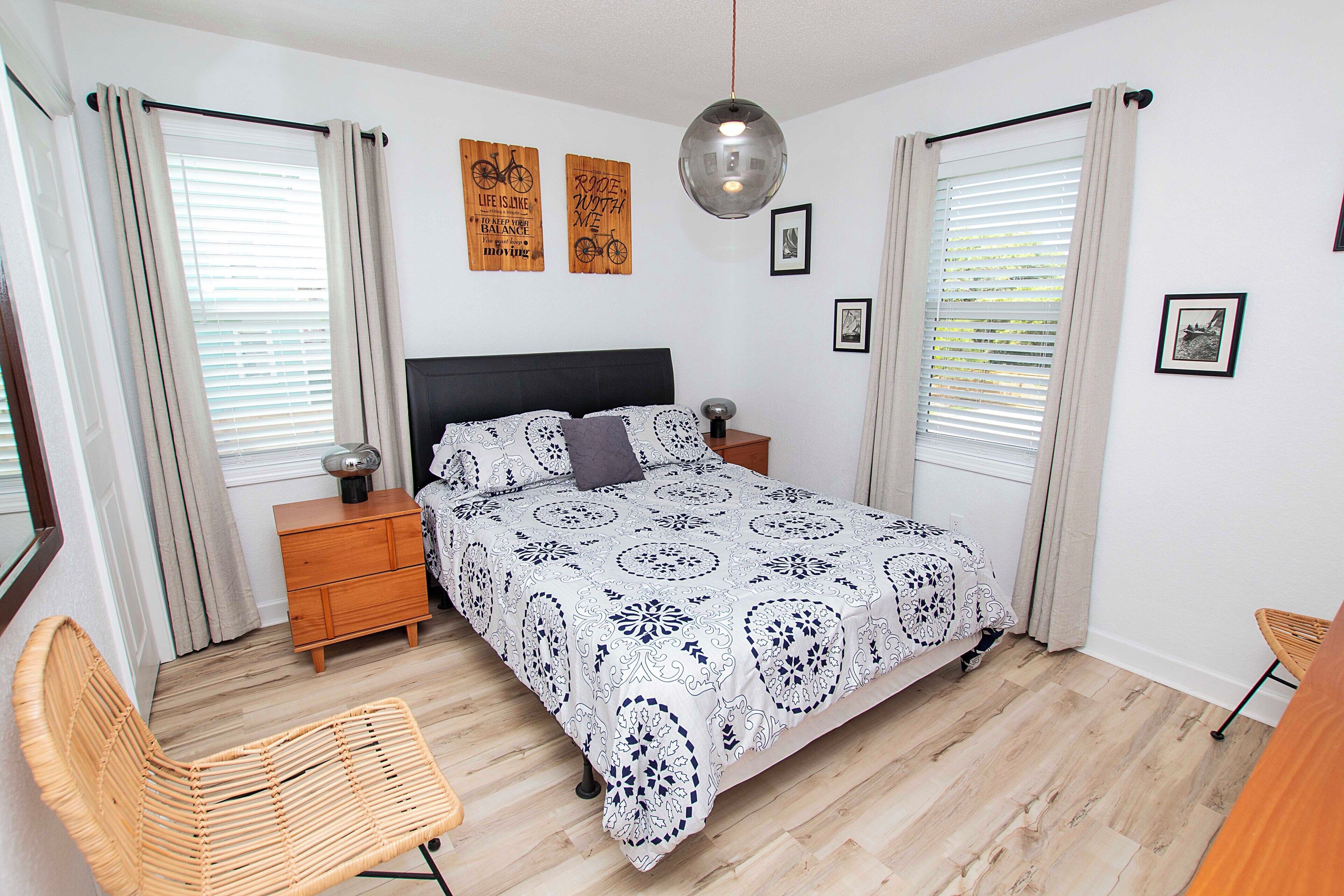 A bedroom with a bed, wooden nightstands, a wicker chair, and a hanging light fixture.