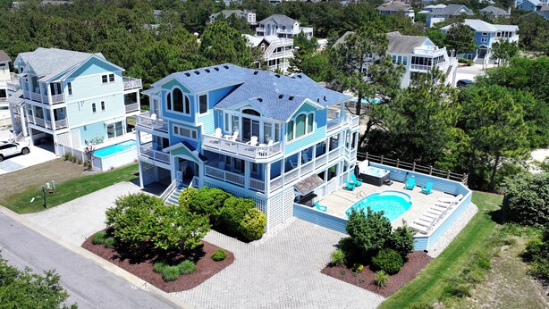 A large two-story house with a swimming pool, surrounded by trees and a view of the ocean.