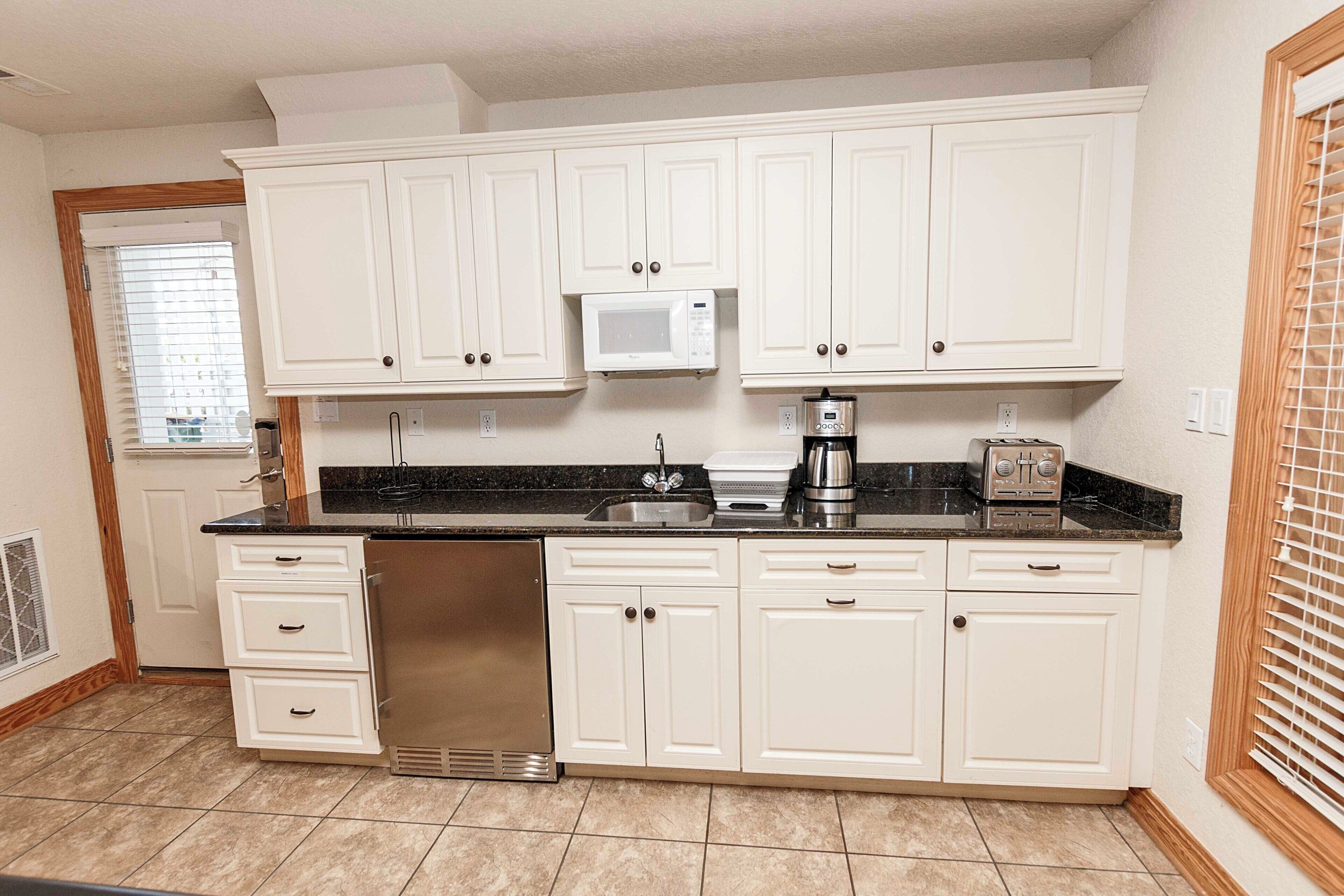 A kitchen with white cabinets, a microwave, a coffee maker, and a toaster.
