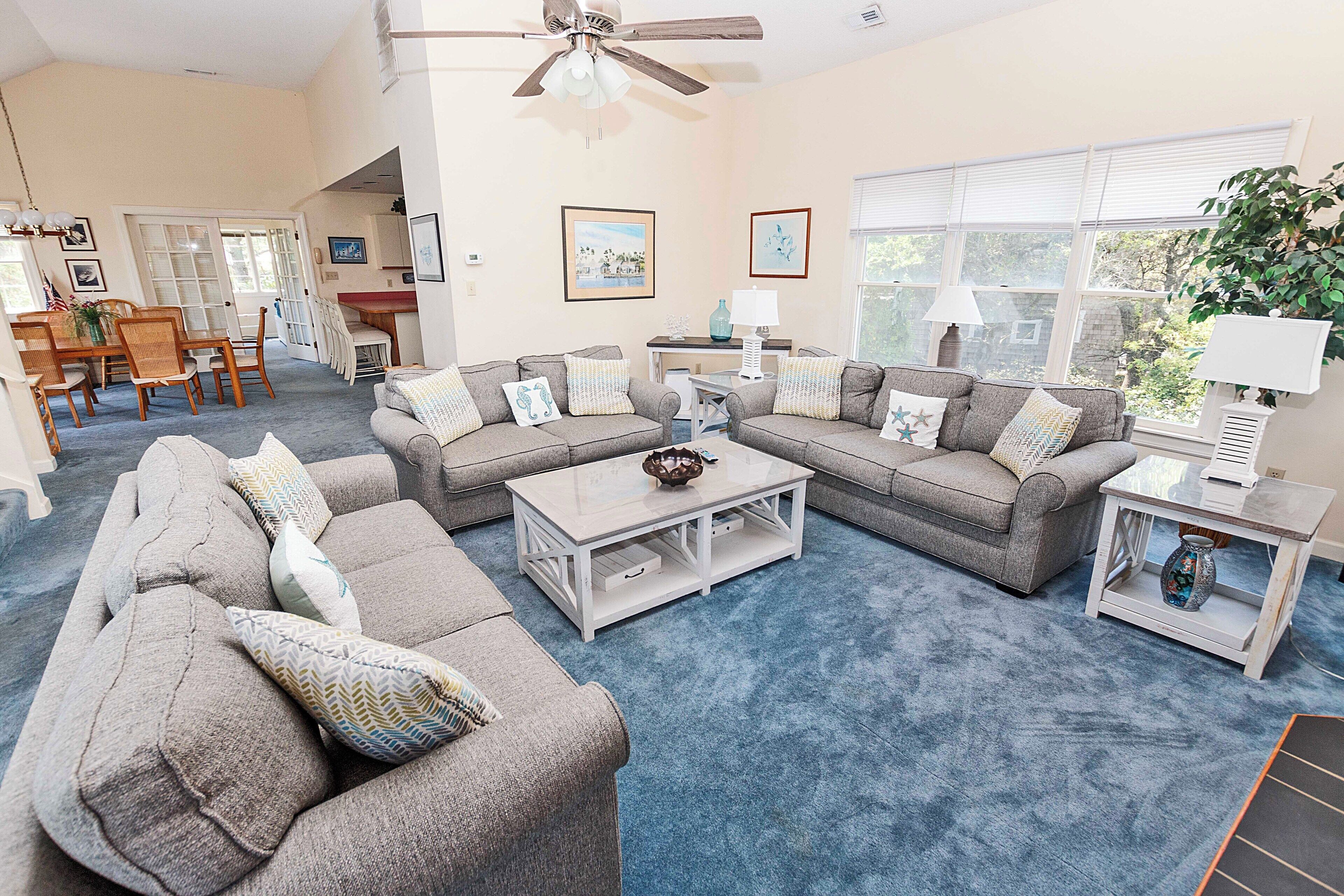 A spacious living room with a large gray sectional sofa, a coffee table, and a dining area with a wooden table and chairs.