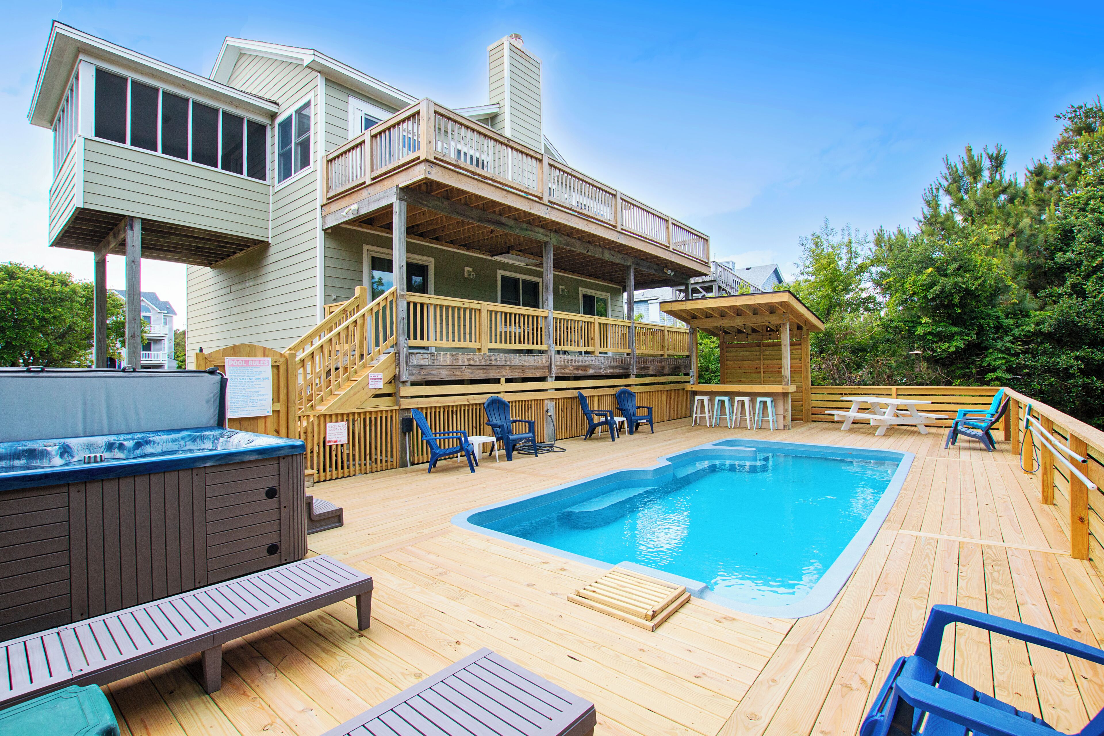A wooden deck with a hot tub, pool, and outdoor seating area.