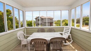 A covered patio with a wooden table and chairs, large windows, and a view of a house. - Oceanside, Pool, Hot Tub, Rec Rm, WC1005, Happily Ours (Corolla)