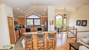 A spacious kitchen with wooden cabinets, a central island with bar stools, a dining area with a table and chairs, and a staircase leading to an upper level.