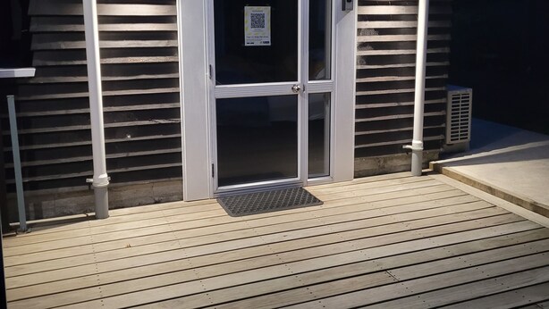 A wooden deck with a glass door entrance, a metal vent, and a QR code sign.