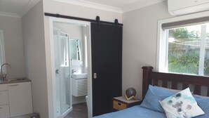 A bedroom with a bed, a bedside table, a window, and a bathroom visible through an open door.