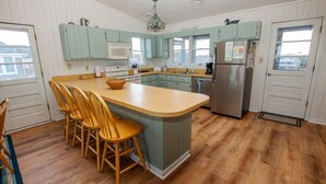 A kitchen with a central island, wooden chairs, a stainless steel refrigerator, and teal cabinets. - OCEANFRONT, Ocean Views, Sun Decks, Close to Beach Access, SA47, Lazy Bones (Duck)