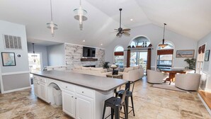 A spacious kitchen with a large island, white cabinetry, and a dining area with a table and chairs. - Oceanside, Pool, Poolside Bar, Sun Decks, WC803, Believing is Sea-ing (Corolla)