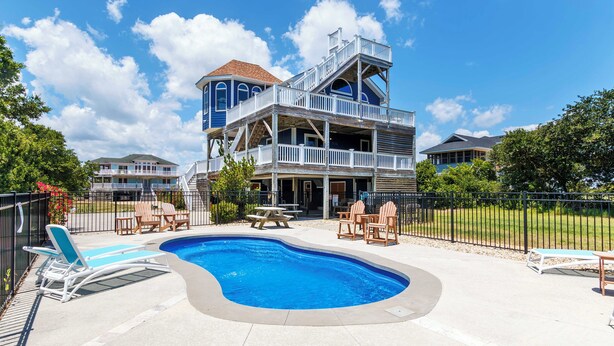 A pool area with lounge chairs and a picnic table, surrounded by a fenced deck and a two-story building with balconies. - Oceanside, Pool, Poolside Bar, Sun Decks, WC803, Believing is Sea-ing (Corolla)