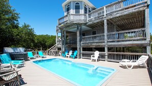 Una terraza de madera con piscina, varios niveles de balcones y mobiliario exterior.