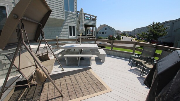 A deck with picnic tables and chairs, a swing set, and a view of neighboring houses. - Oceanside, Community Pool, Community Amenities, 677, Windswept II (Corolla)