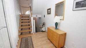 A hallway with a wooden staircase, a wooden cabinet, a mirror, and a lamp. - Oceanside, Community Pool, Community Amenities, 677, Windswept II (Corolla)