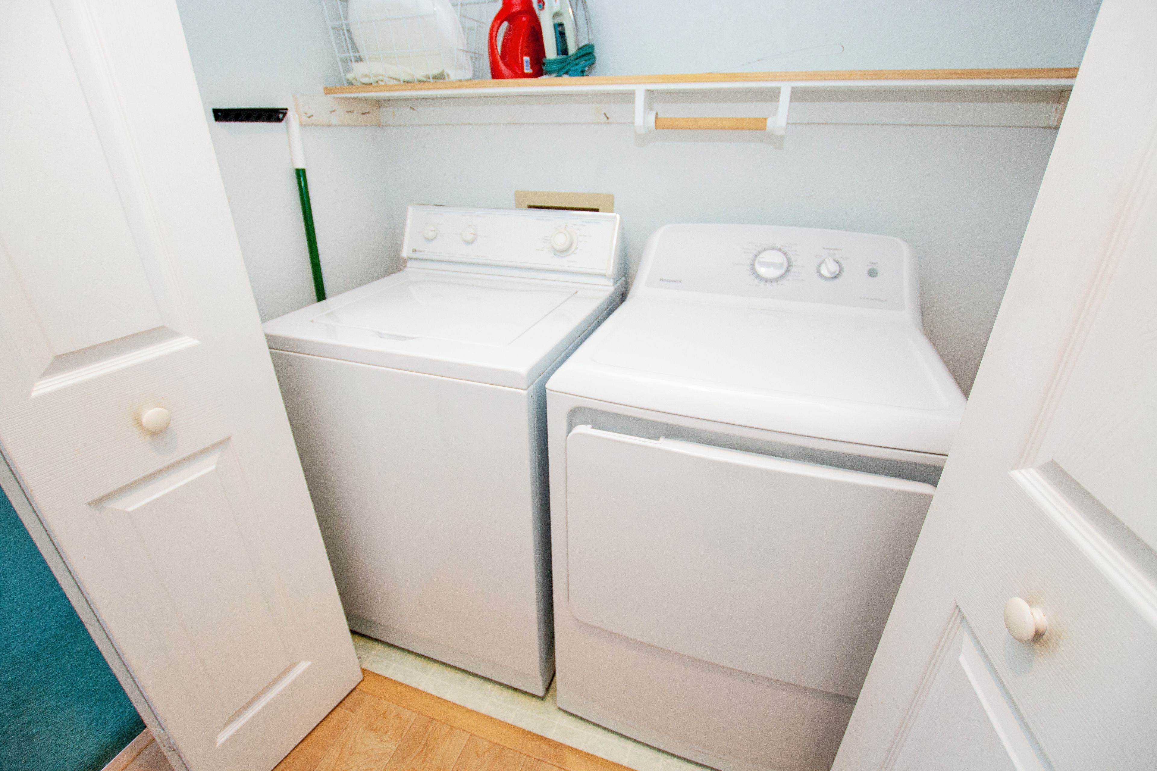 A laundry room with two white washing machines and a shelf above them.